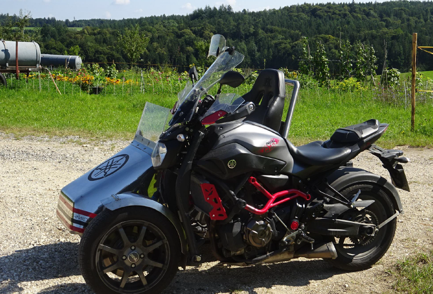 Ein Motorrad mit Beiwagen, geparkt auf einer Schotterstraße, umgeben von Grün.